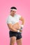 A funny fat man with dubbell isolated on pink background. Obesity and eating disorder. Concept for dietetics and fitness