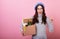 Funny French lady in a stylish beret hat, with a cardboard box in her hands on a pink background