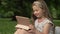 Funny girl 6-7 years old sits on the grass in a summer park with a tablet. Children learn gadgets easily. Modern