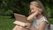 Funny girl 6-7 years old sits on the grass in a summer park with a tablet. Children learn gadgets easily. Modern