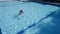 A funny girl bathing in swimming pool outdoors and playing with cute yellow inflatable duck swims behind her and catches