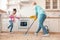 Funny girl jumping while mother mopping the floor near her