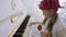 Funny girl in red hat playing music on piano and holding lollipop in hand