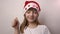 Funny girl in Santa Claus hat smiles, laughs, pulls approving thumbs up sign