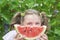 Funny girl with slice of watermelon looks into the camera with big eyes. Summer time concept, happiness, childhood. Selective