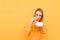 Funny girl standing with a pack and burger on a yellow background and eating, wearing an orange sweatshirt. Cute girl cheer fast