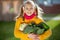 Funny girl with two pigtails in yellow smiling with fresh autumn harvest in sunny rural garden