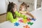 Funny girls collect puzzles together at the table in the children`s room