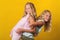 Funny girls twins have fun together on yellow background.