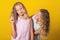 Funny girls twins have fun together on yellow background.