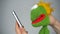 Funny green puppet looking in smartphone