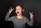 Funny grimacing kid girl listening the music, singing in wireless headphones and showing the hands v sign on grey dark background