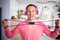Funny grimacing man working out with small pink dumbbells at home