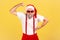 Funny grumpy man in santa claus hat and pants with suspenders showing his arm muscles seriously looking at camera through red