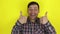 Funny handsome guy smiles and shows thumb up with both hands. Portrait on yellow background.