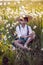 funny happy a beautiful boy child sit in hat on a field with white dandelions at sunset in summer. soap bubbles are