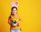 Funny happy child girl with easter bunny ears and with spring flowers tulips on yellow