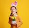 Funny happy child girl with easter bunny ears and with spring flowers tulips on yellow