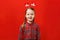 Funny happy child in a red christmas dress and mittens on his head. Little girl smiles on a colored background. Copy space