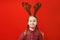 Funny happy child in red christmas dresse and deer horns on his head on a colored background. Emotional little girl in delight.