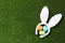 Funny headband with Easter bunny ears and dyed eggs on green grass, flat lay.