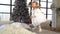 Funny jumping little girl dressed in white dress with Christmas tree behind her