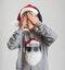 Funny kid boy in Christmas Santa hat and sweater closed his eyes with hands. Smiling face waiting for surprise. Child