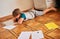 Funny kid boy doing school homework, lying on the floor