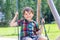 Funny kid boy having fun with chain swing on outdoor playground during rain. child swinging on warm rainy summer day