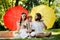 Funny kids with mom and dad sitting on the blanket under the big red and yellow umbrellas covering them from the sun.