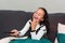 Funny latin girl laughing and watching TV at the sofa with remote control on his hand