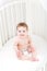 Funny laughing baby wearing a diaper sitting in a white round crib