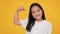 Funny little asian girl showing biceps, demonstrating tiny muscles, smiling to camera over orange studio background