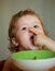 Funny little baby in the kitchen eating with fingers from plate. Funny child face closeup.