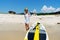 Funny little boy posing at beach sand coast near sup surfboard performing shaka gesture