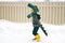 Funny little child in homemade cardboard textile dinosaur or crocodile costume walking on snowy road