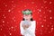 Funny little girl blowing a multi color paper spray in her hands against floating snow on red christmas background. A moment of