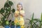 Funny little girl gardener with plants in the room at home.