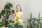 Funny little girl gardener with plants in the room at home.