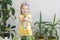 Funny little girl gardener with plants in the room at home.