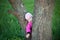 Funny little girl hides behind tree