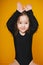 Funny little girl make bunny ears by hands on orange background. Copy-space