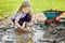 Funny little girl playing in a large wet mud puddle on sunny summer day. Child getting dirty while digging in muddy soil.