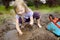 Funny little girl playing in a large wet mud puddle on sunny summer day. Child getting dirty while digging in muddy soil.