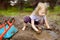 Funny little girl playing in a large wet mud puddle on sunny summer day. Child getting dirty while digging in muddy soil