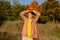 Funny little girl standing in autumn forest during sunset, holding orange pumpkin over her head.