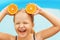 Funny little girl swimming in the pool. The child holds the halves of the orange instead of the ears. Summer concept.