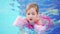 a funny little girl swims and plays in inflatable armbands in a pool