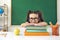 Funny little schoolgirl in glasses sitting in a lesson in class in school.