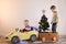 Funny little smiling kids driving toy car with Christmas tree. Happy child in colour fashion clothes bringing hewed xmas tree from